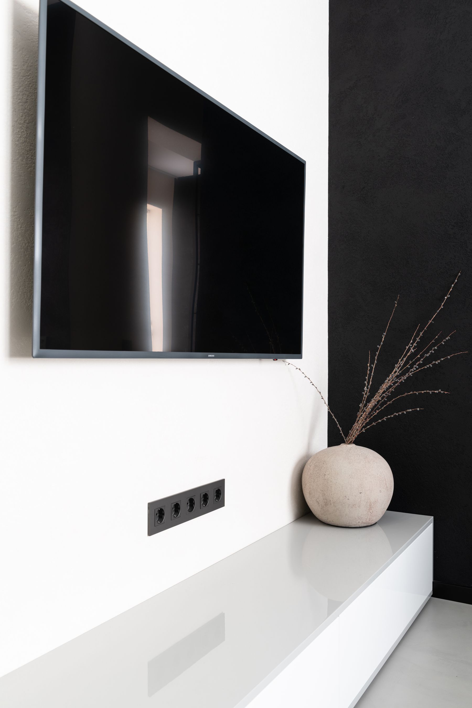 Television mounted on white wall above a round vase