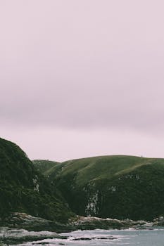 Peaceful coastal landscape featuring rolling green hills and overcast skies.