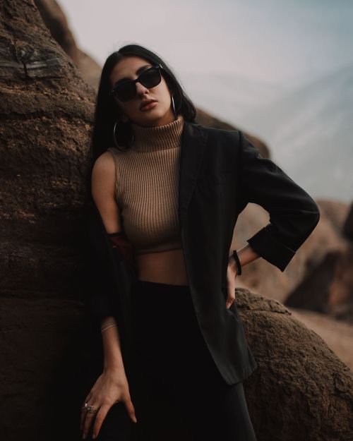 Free Stylish woman in sunglasses and blazer posing against rock formations in a moody setting. Stock Photo