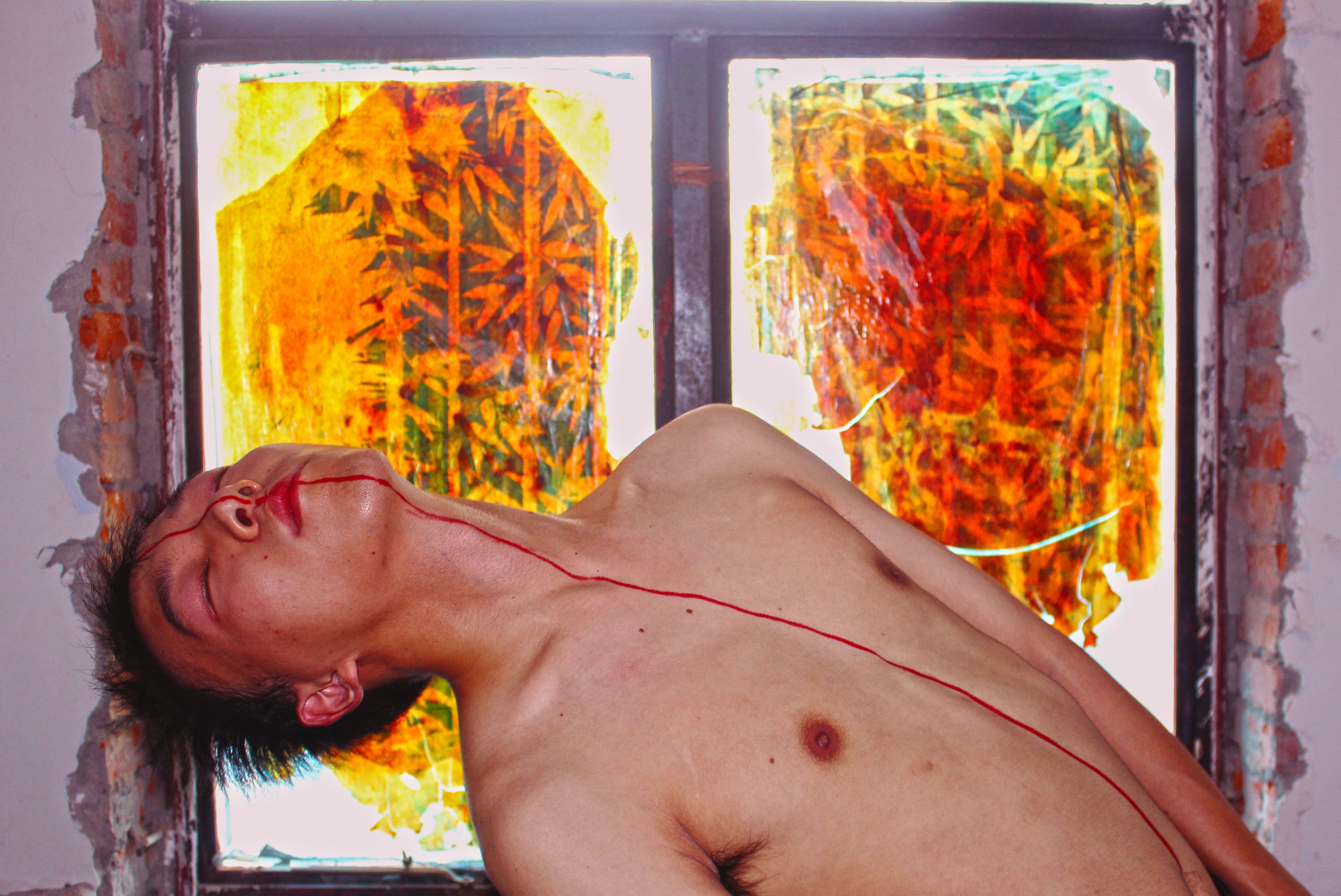 Abstract portrayal of a topless man with body paint in front of colorful window art.