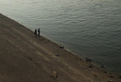 2 человека идут по коричневому песку возле водоема