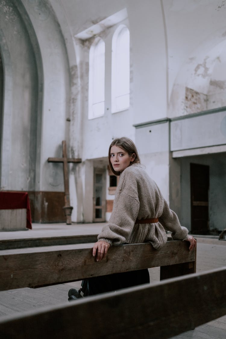 A Woman Sitting On A Pew In An Abandoned Church