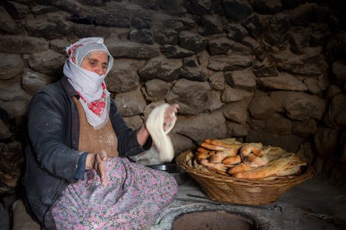 Woman Holding Dough Sitting Near a Basket of Bread