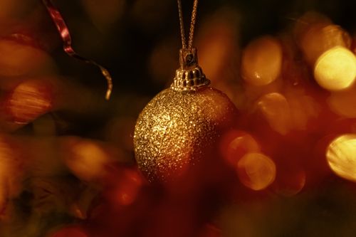 Free A sparkling golden ornament on a Christmas tree surrounded by warm bokeh. Stock Photo
