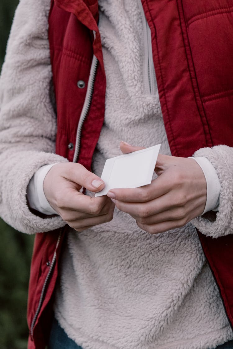 Person In Beige Fleece Sweater And Red Vest Jacket Holding A Card