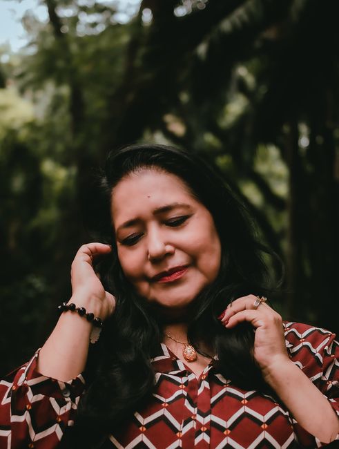 A woman enjoys a peaceful moment outdoors, smiling with eyes closed, surrounded by nature.