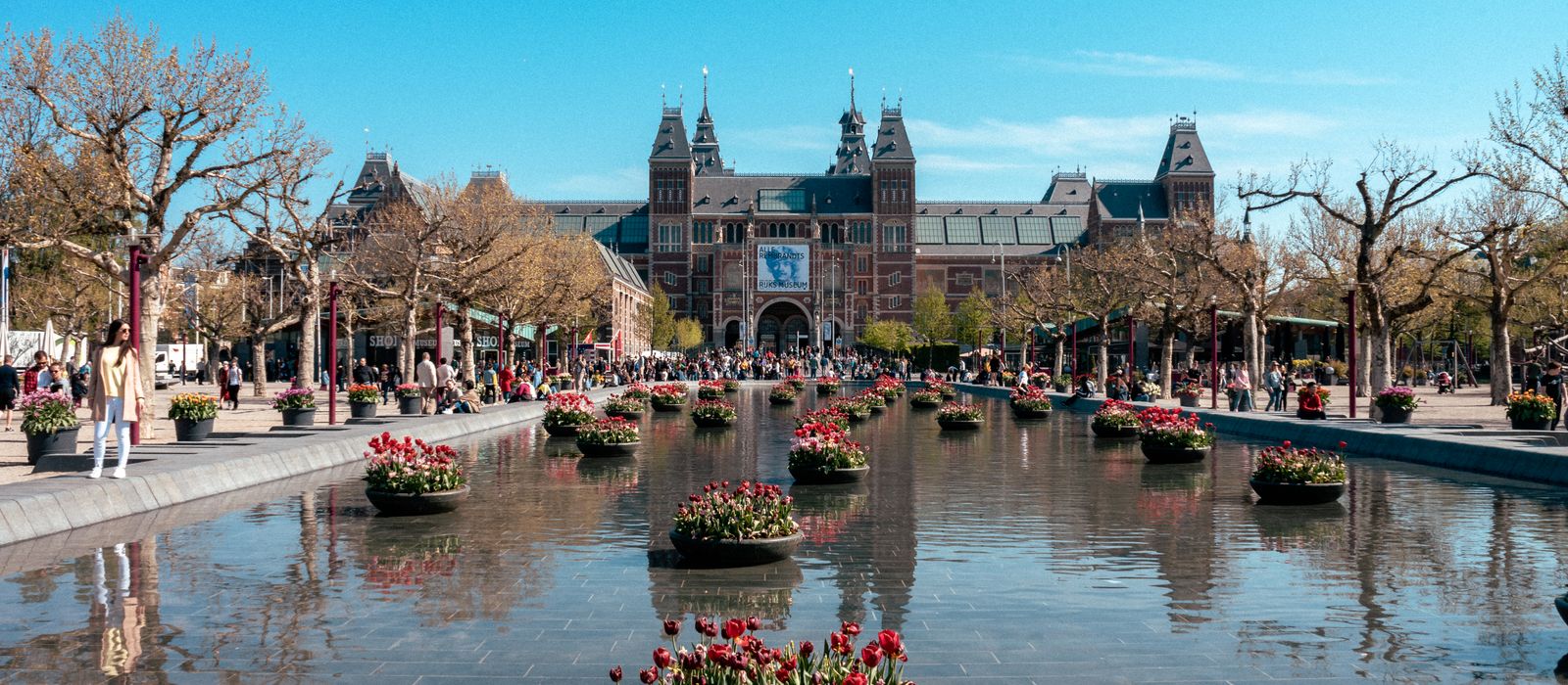Rijksmuseum view in Amsterdam with tulip planters and a reflective pond, highlighting its iconic architecture.