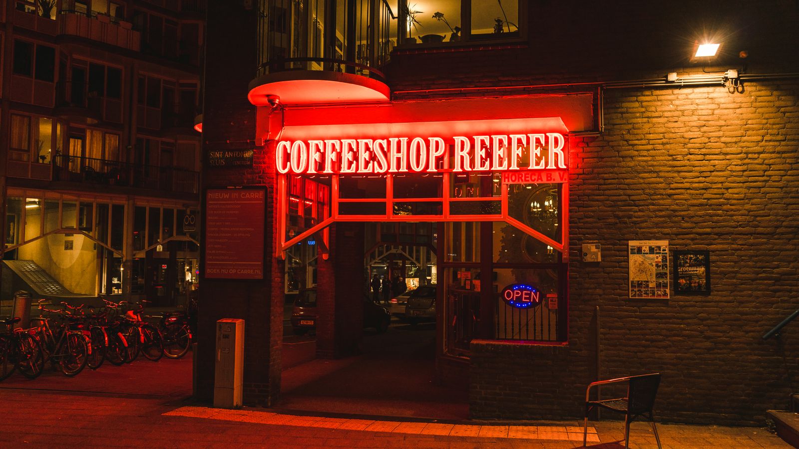 Nighttime view of Coffeeshop Reefer's vibrant neon entrance in Amsterdam, Netherlands.