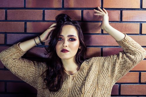 Free Fashionable portrait of a woman with long hair and makeup posing by a brick wall in Warsaw. Stock Photo