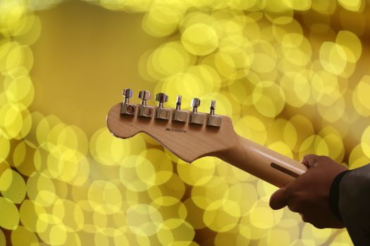Close-up of an electric guitar head with golden bokeh lights in the background, creating a vibrant and artistic scene.