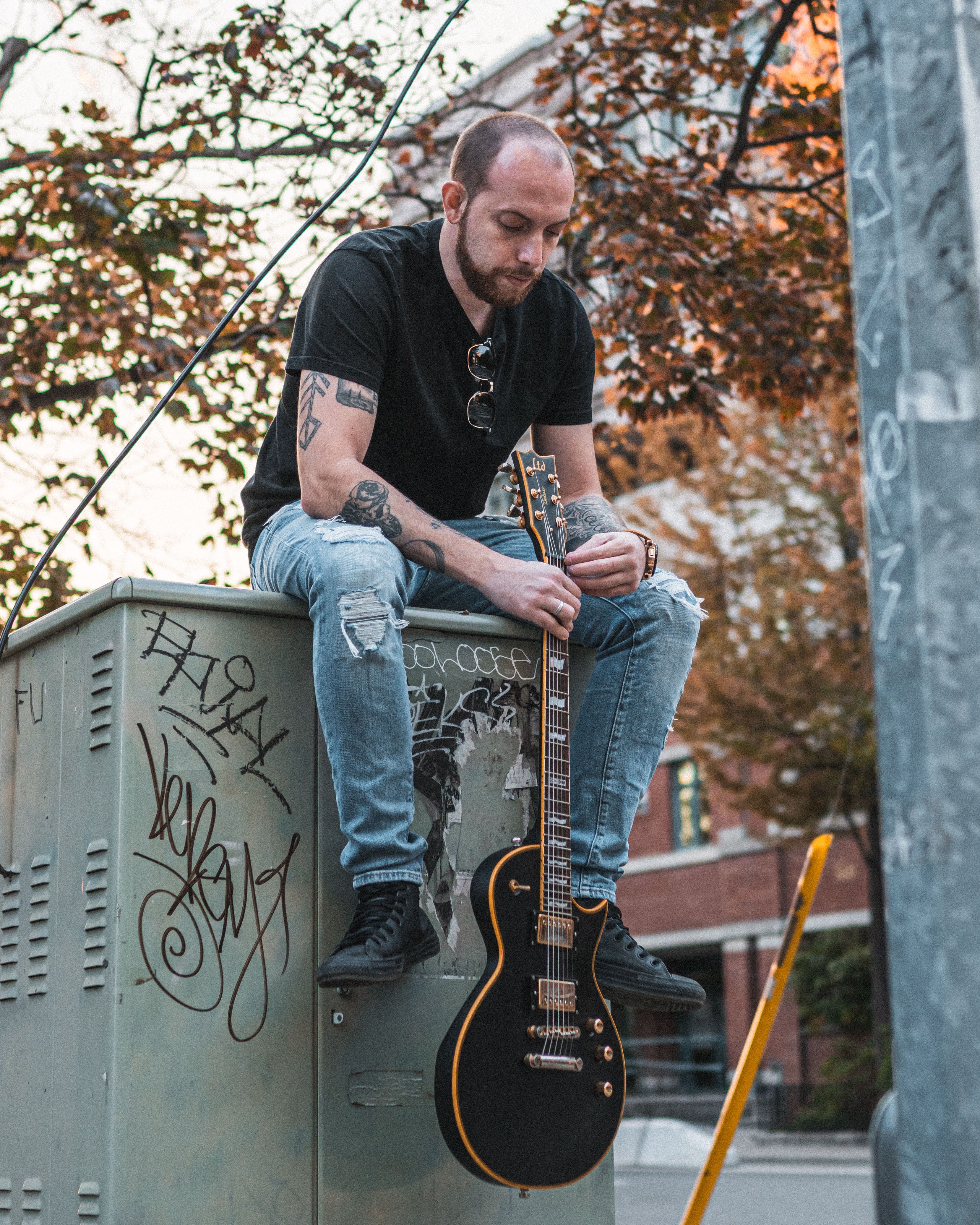 A street musician sitting on a graffiti-covered box with his electric guitar in Toronto.