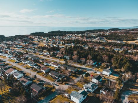 From above of small settlement with typical residential houses and green trees located on seashore under cloudy bly sky on sunny day in autumn