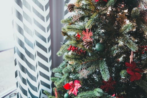 Christmas tree decorated with toys standing near window with patterned curtain on daylight in winter