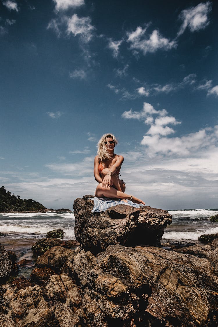 Female Traveler On Boulder Against Foamy Sea