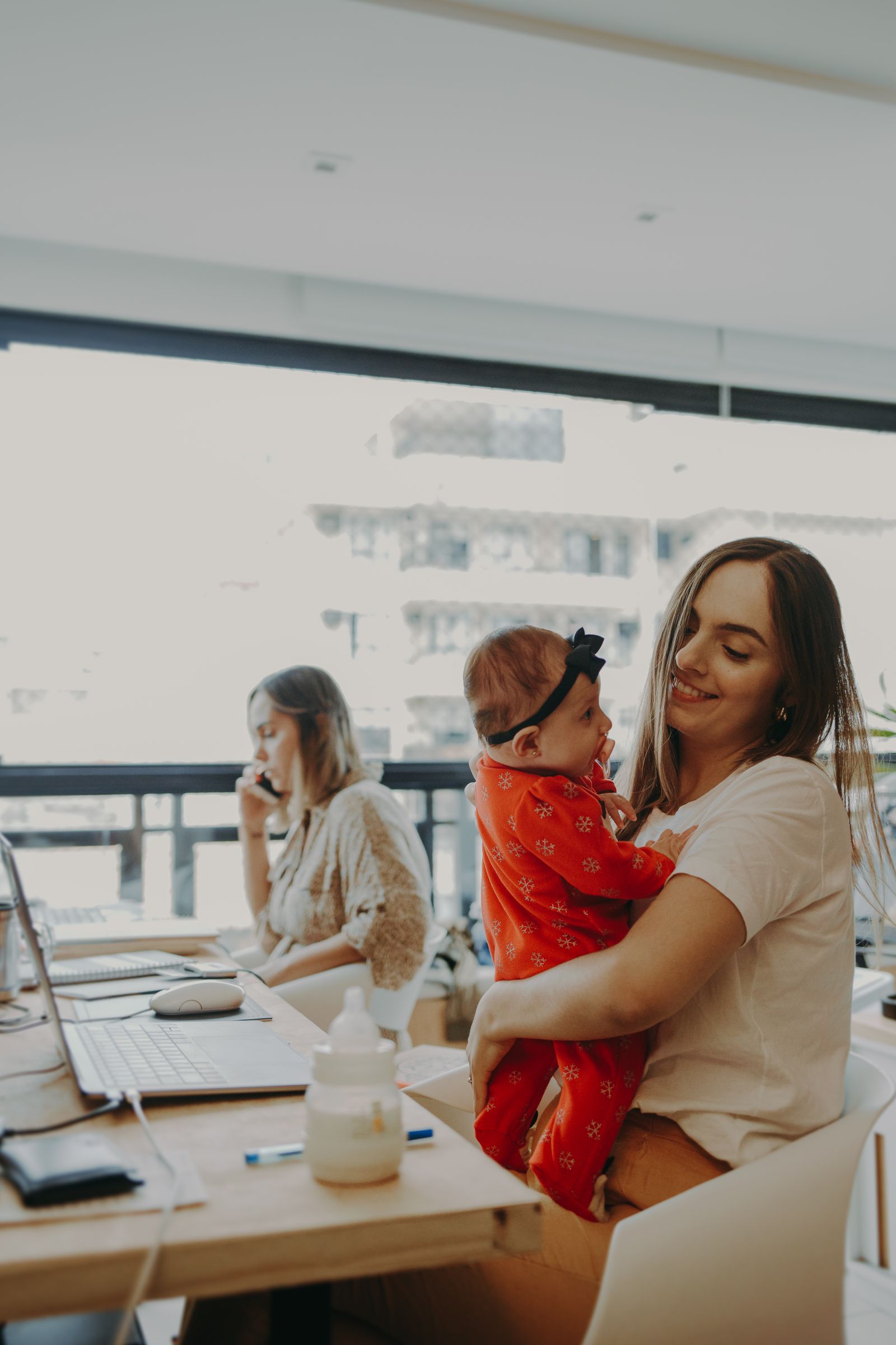 Mother holding her toddler while working, illustrating the strain of balancing childcare and work