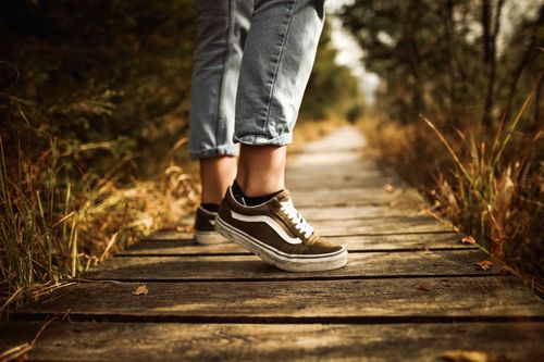 Free Close-up of a person walking on a wooden path in a park wearing jeans and sneakers during autumn. Stock Photo