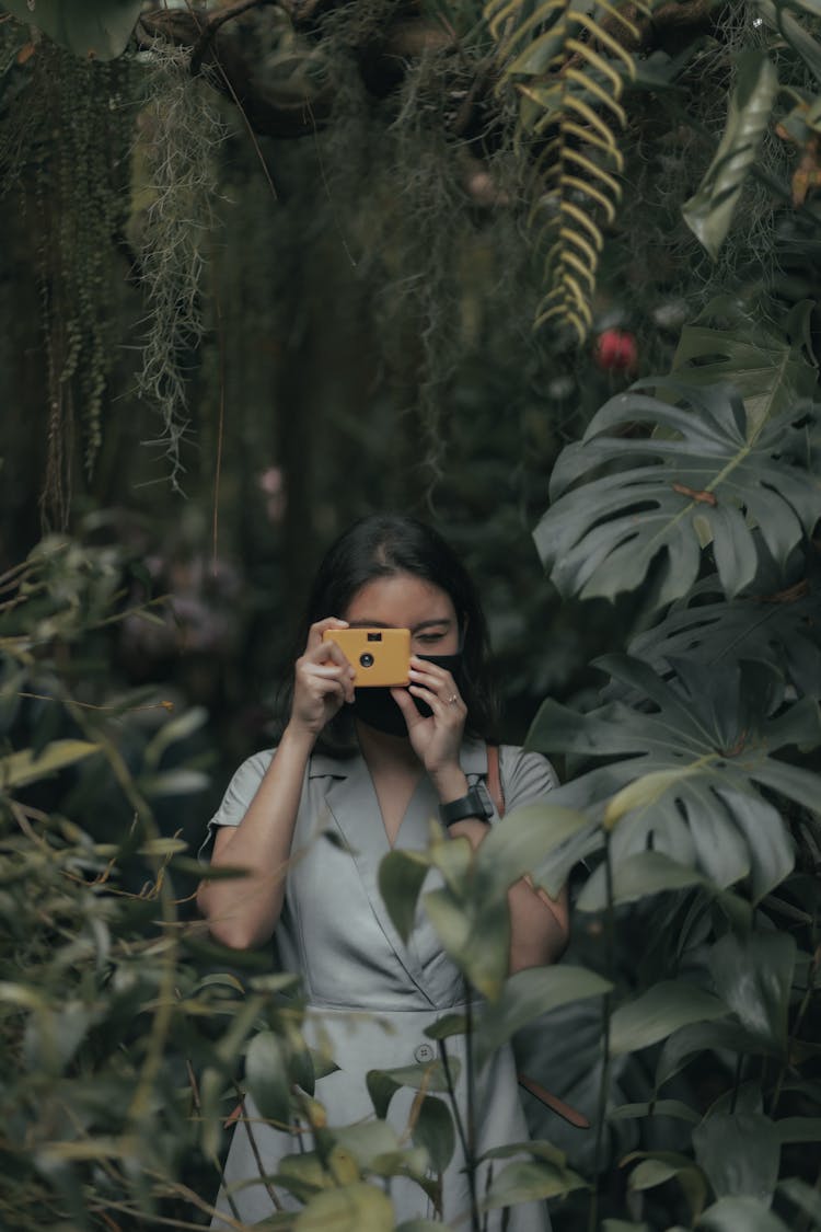 Faceless Woman Near Plants Taking Photo With Film Camera