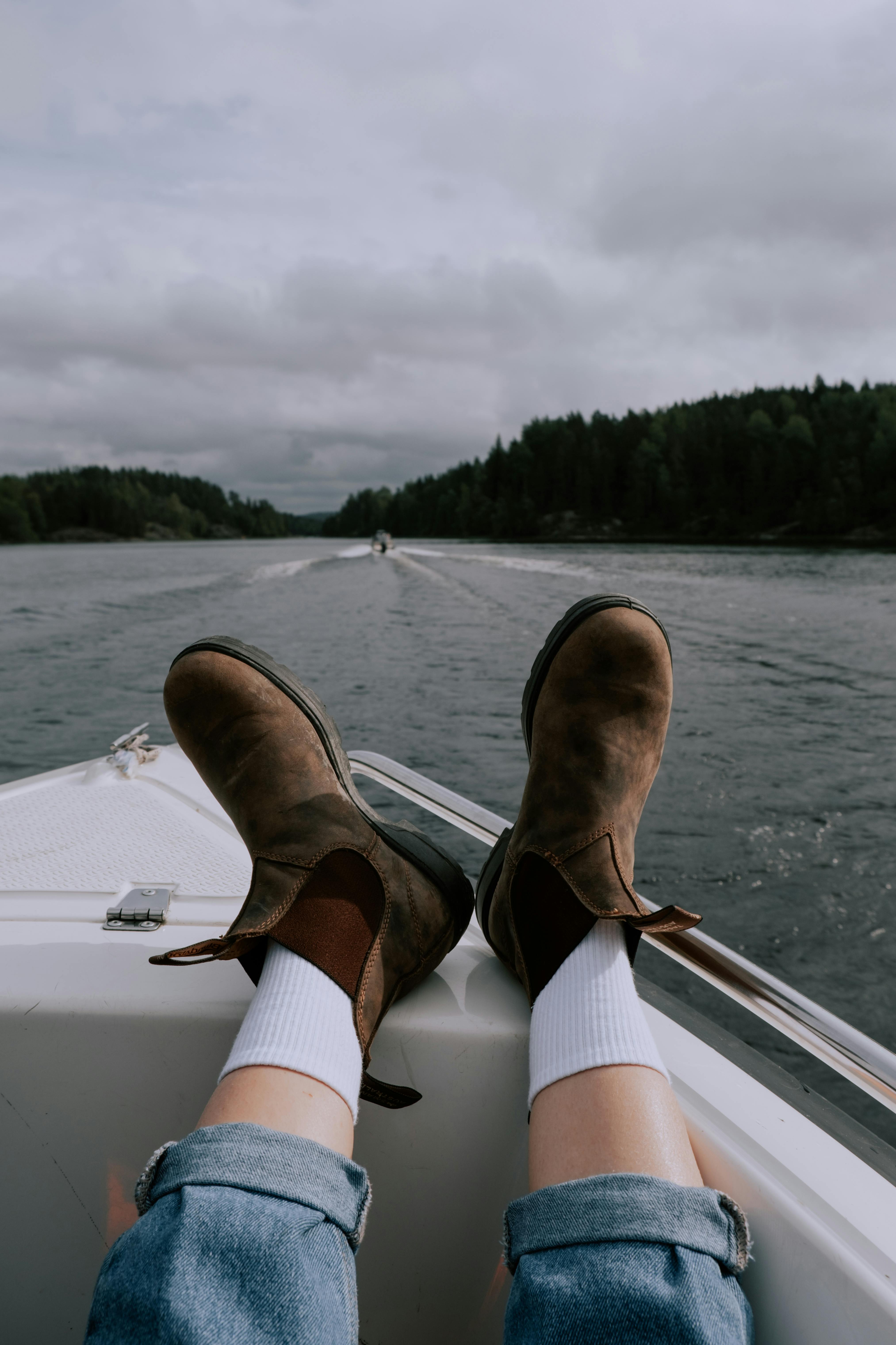 Person relaxing in brown boots on a boat, enjoying a serene lake view.
