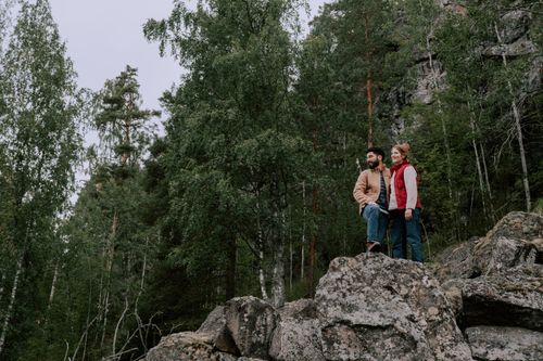 Free A couple enjoys hiking through a lush forest, standing on rocky terrain. Stock Photo