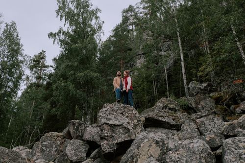 Free A couple stands on rocky terrain surrounded by lush forest, embracing the beauty of nature. Stock Photo