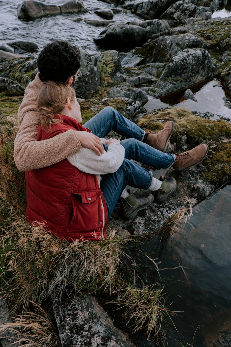 Couple Sitting On Rock Near Body Of Water