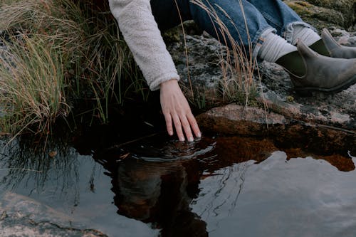 Person Sitting on Rock Touching Water