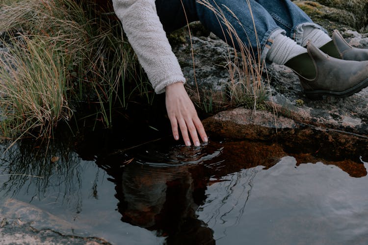 Person Sitting On Rock Touching Water