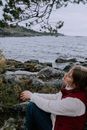 Woman in White Jacket Sitting on Rock Near Body of Water