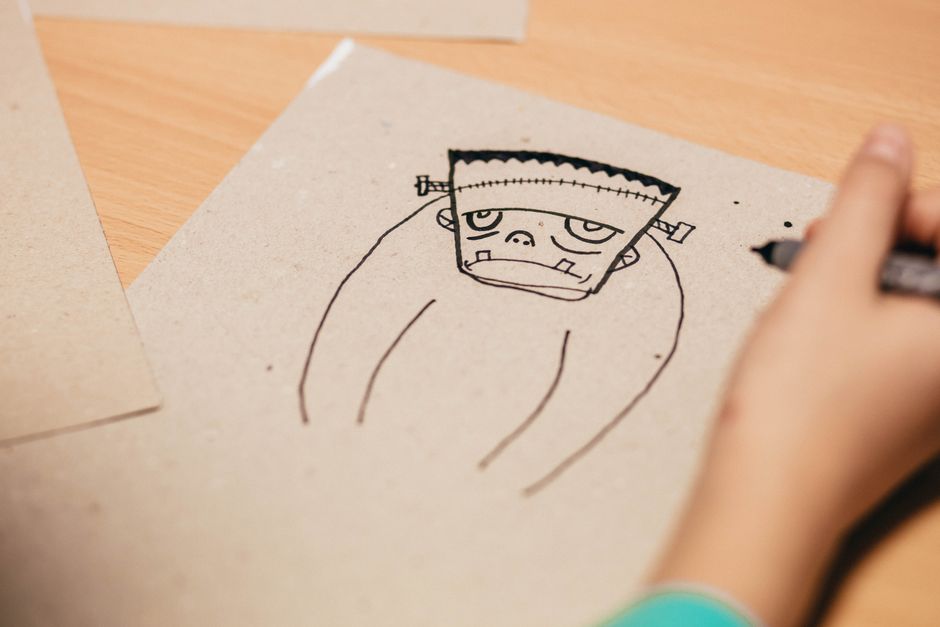 Fotomural Primer plano de un niño dibujando un personaje de dibujos animados en papel con un bolígrafo negro.