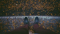 俯瞰秋天的人行道，一个人穿着时尚运动鞋站在铺满落叶的路面上