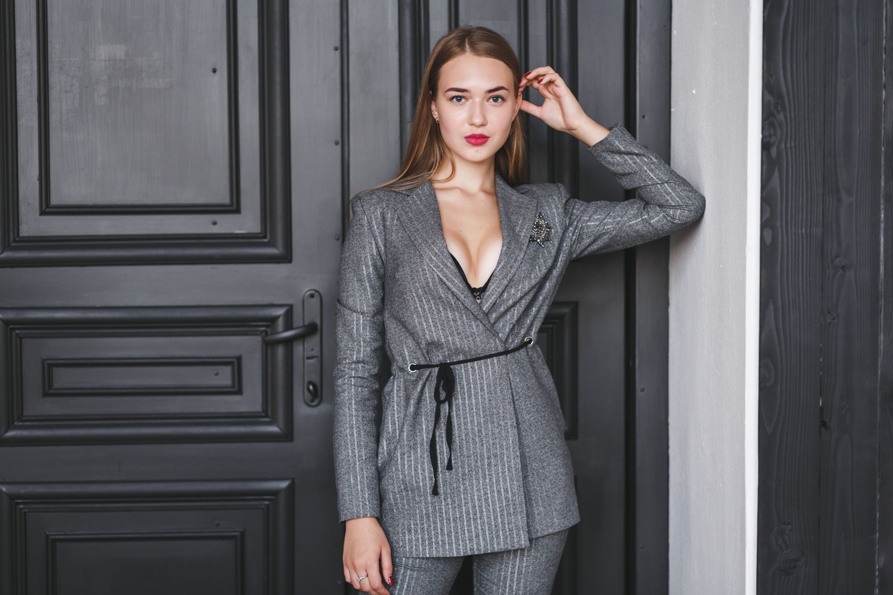 Confident woman posing against a dark door in a stylish gray suit.