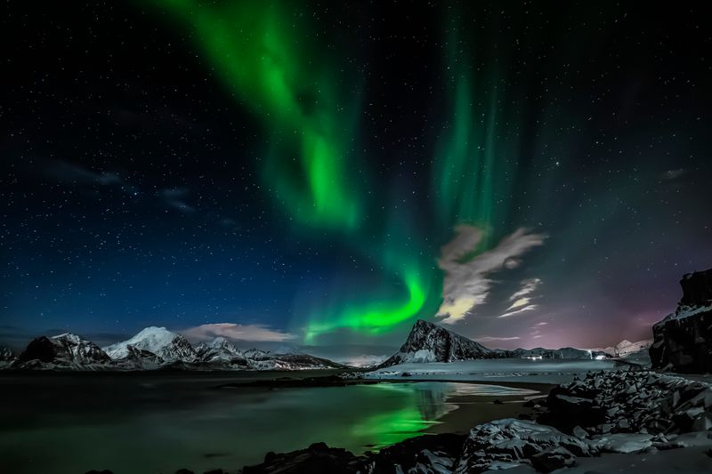 Aurora boreală deasupra munților înzăpeziți noaptea