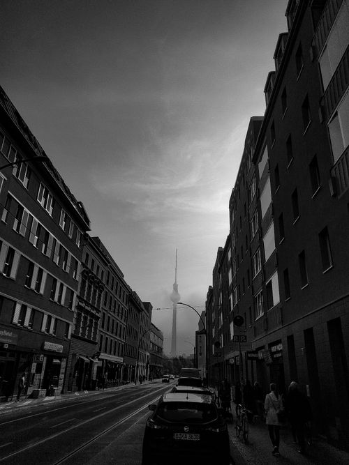 Free Black and white photo of urban street leading to a tower, with parked cars and moody clouds. Stock Photo