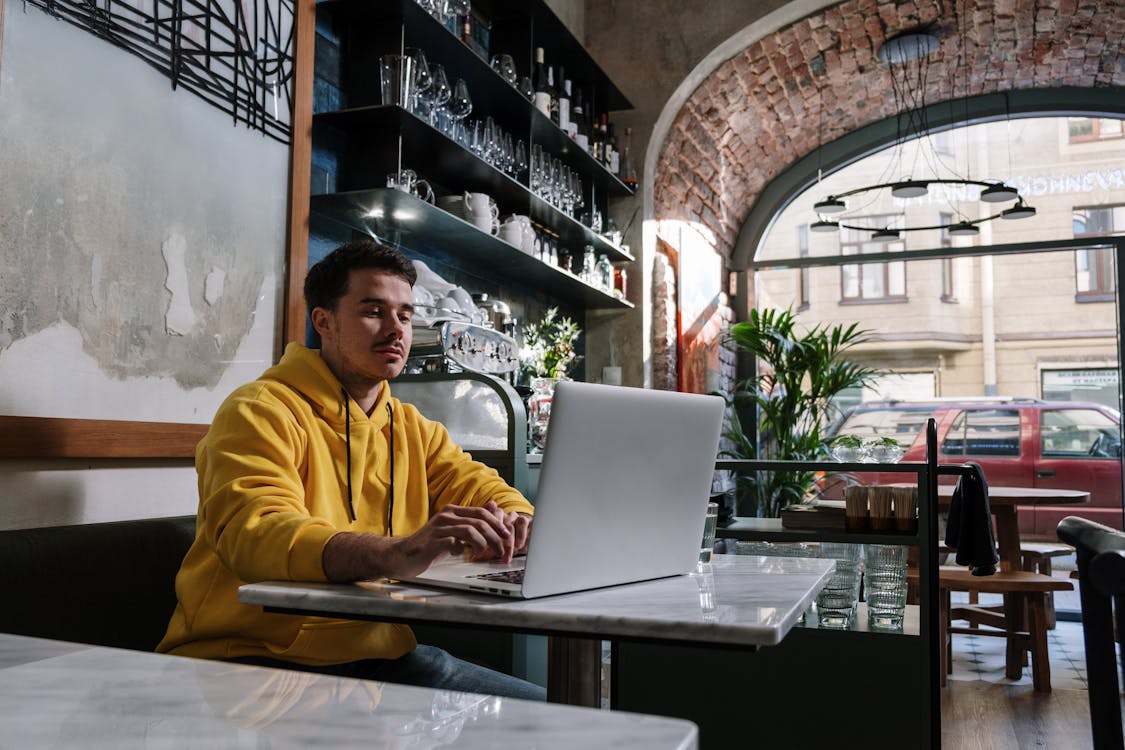 Photo of a Man in a Yellow Hoodie Working on His Laptop
