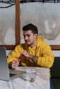 Man in a Yellow Hoodie Looking at His Laptop