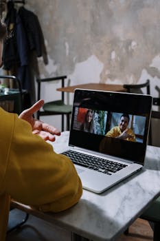 Person in a yellow sweater hosting a video call on a laptop indoors.