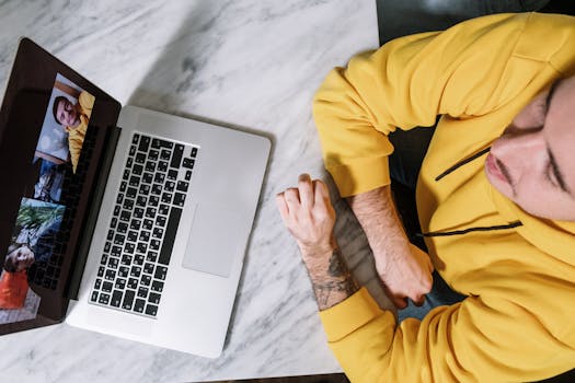 Man in yellow hoodie participating in a virtual meeting using a laptop on a marble table.