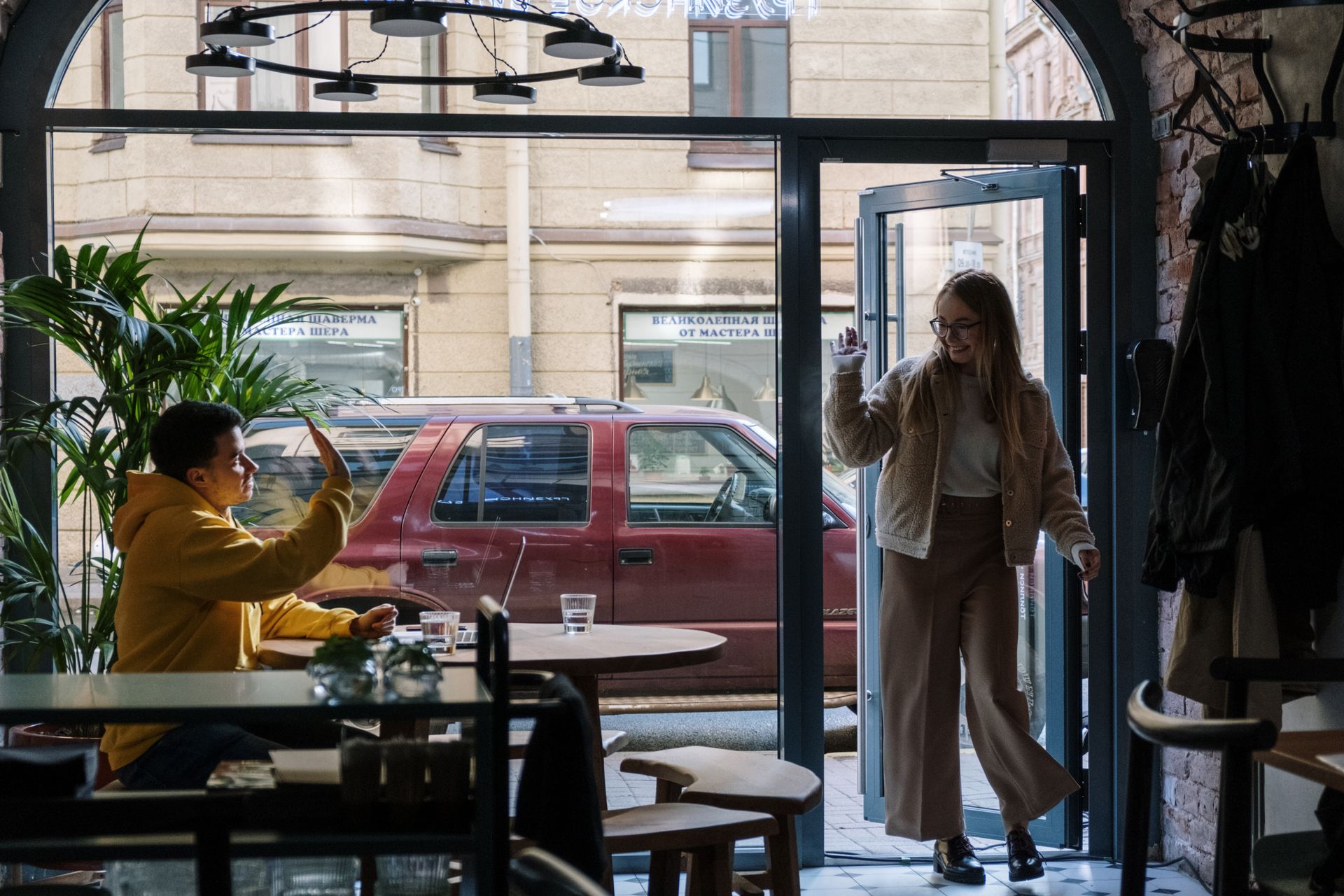 A woman enters a cozy cafe to greet a friend, creating a warm and inviting atmosphere.