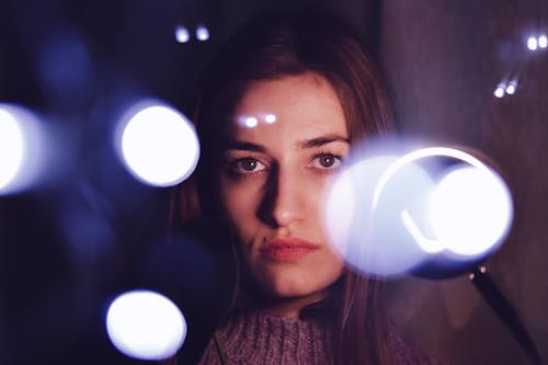 Free Thoughtful young ethnic lady looking at camera amidst glowing lights Stock Photo