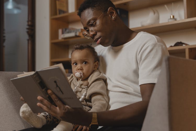 A Man Reading  Book To A Baby With Pacifier