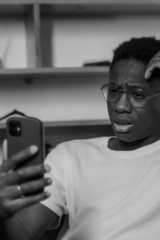 African American man with glasses looking at cellphone with a puzzled expression in black and white.