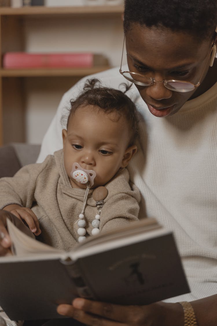 Man In White Crew Neck T Shirt Reading A Book With Baby