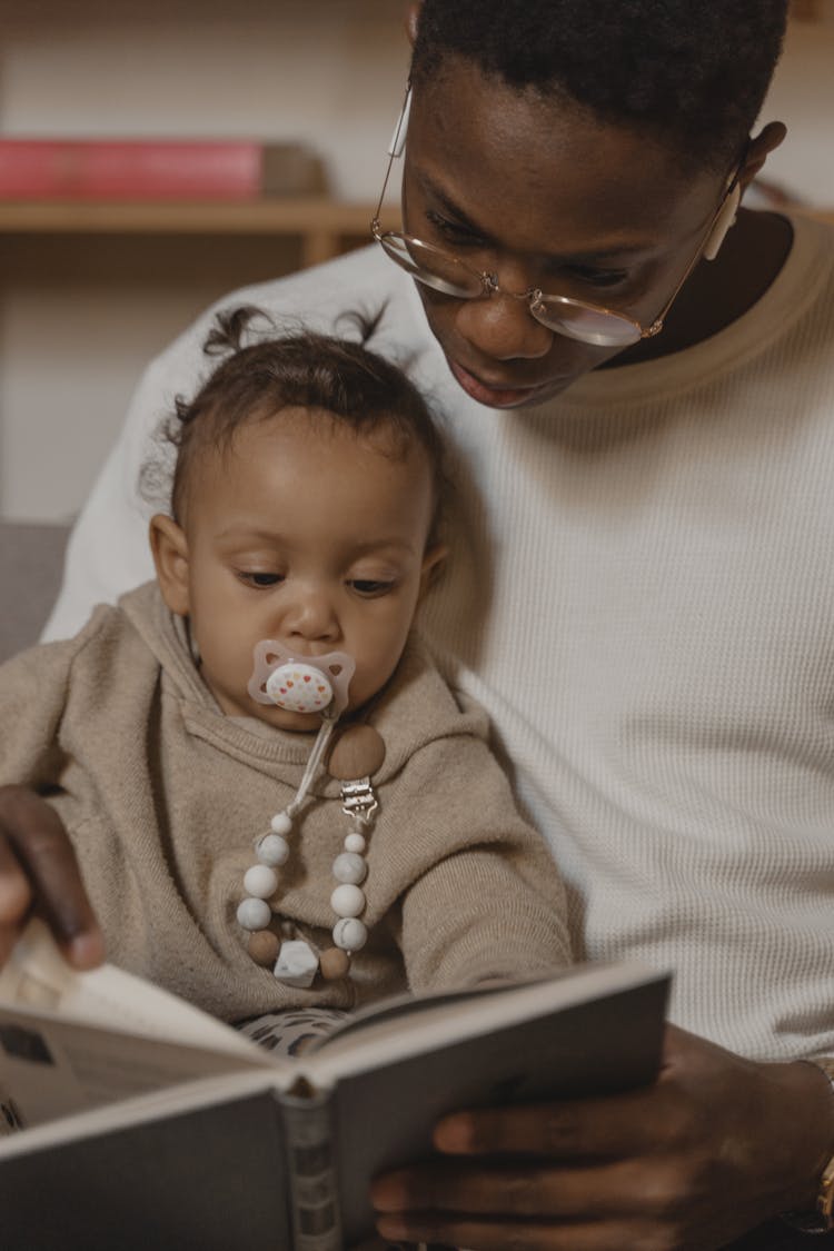 A Man Reading A Book To A Baby With Pacifier