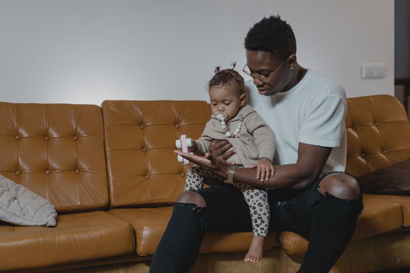 A father lovingly holds his baby on a leather sofa. Cozy indoor setting captures family bonding.