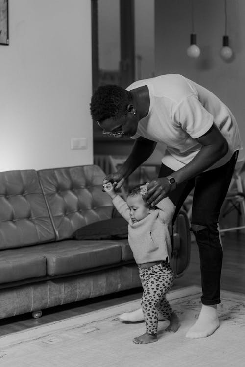 Grayscale Photo of a Man Helping a Toddler Walk