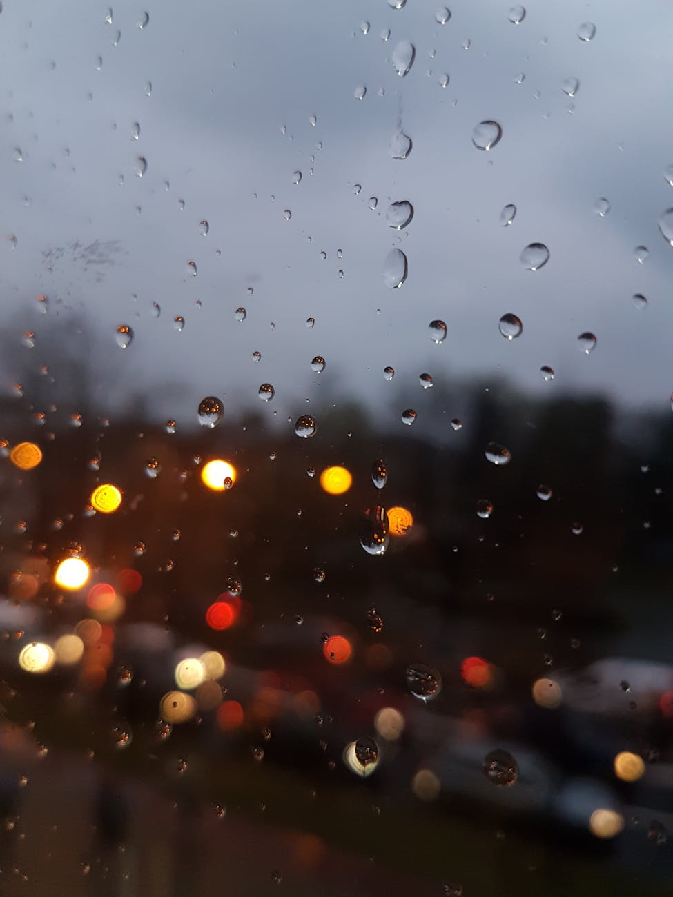 Raindrops on a window with blurred city lights creating a bokeh effect at twilight.