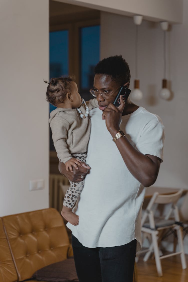 A Man Carrying A Baby Using A Cellphone