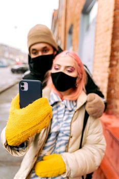 Couple wearing face masks taking a selfie outdoors. Emphasizes pandemic era urban life.