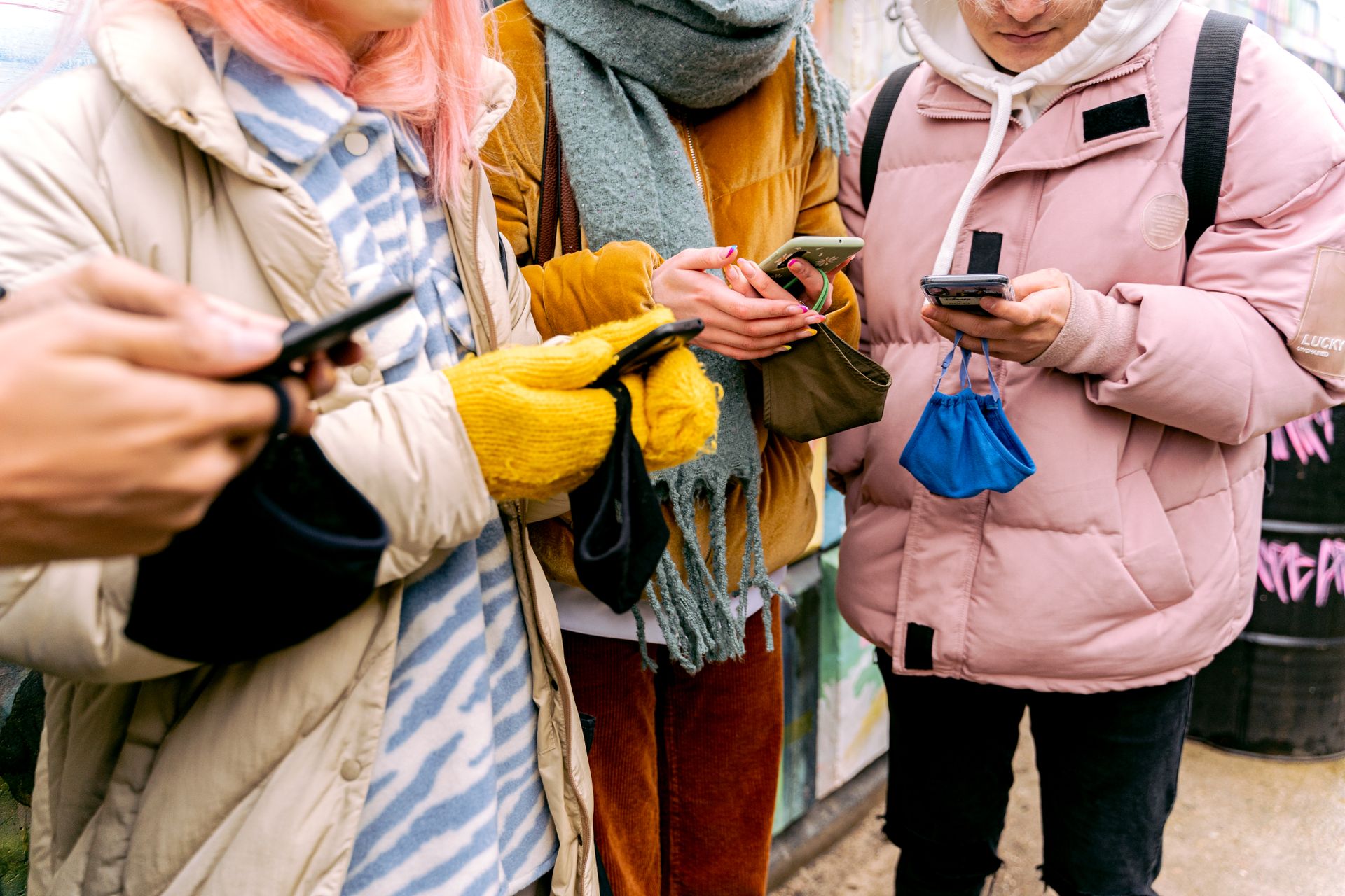 Four people dressed warmly, using smartphones outdoors in a winter setting.