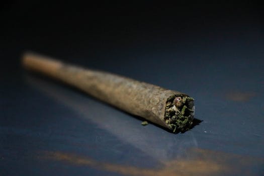 Macro shot of a cannabis joint resting on a dark navy blue surface with selective focus.